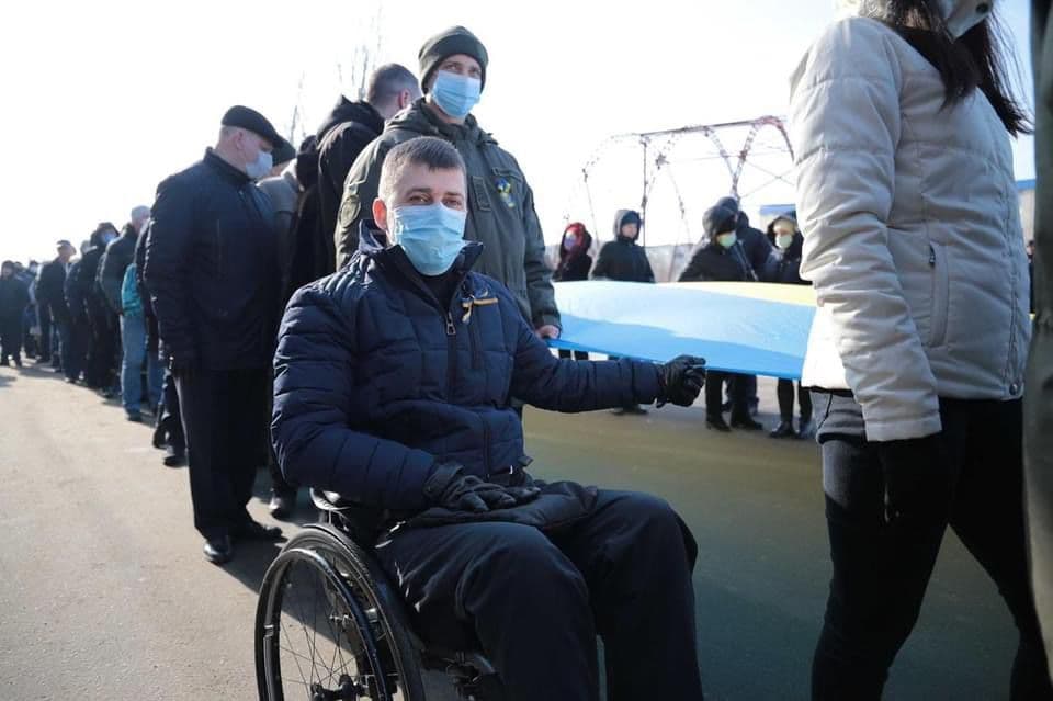 Чоловік сидить, а на задньому плані багато людей тримають великий прапор.