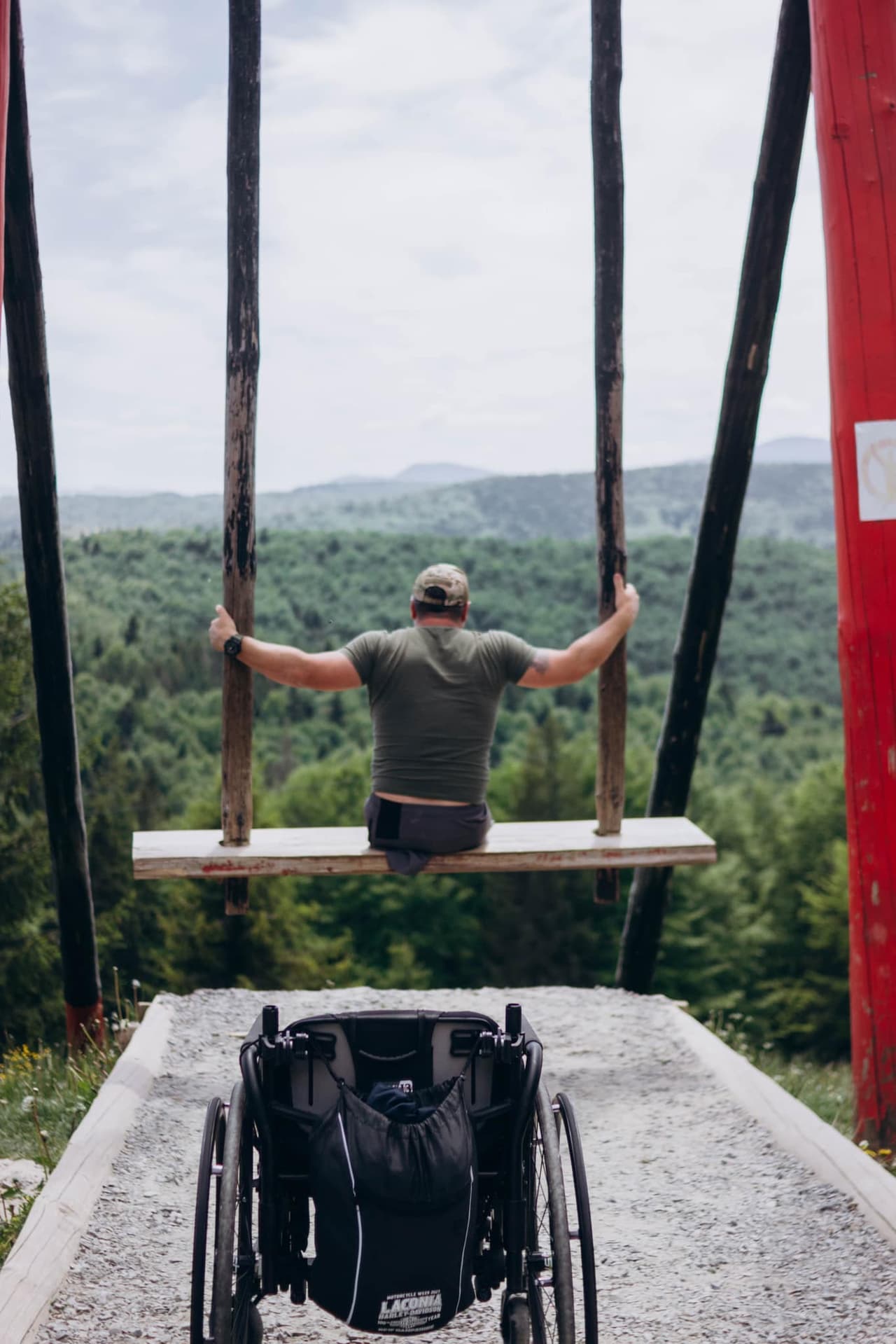 A wheelchair in the foreground, followed by a man swinging on a swing.