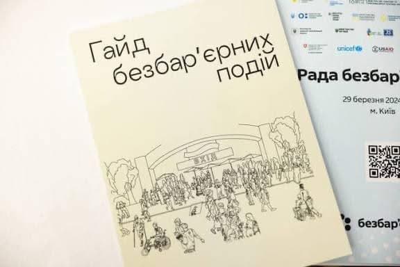 Two printed materials stacked together. The top item is a booklet with a cream-colored cover featuring a line drawing of a crowd in front of a building with trees. The title reads “Guide to Barrier-Free Events.” Beneath it, a partially visible flyer shows logos of organizations including UNICEF and USAID, with text “Council of Accessibility,” the date “29 March 2023,” and location “Kyiv.” A QR code and branding are also present. The scene highlights initiatives promoting accessibility and inclusivity in public events.