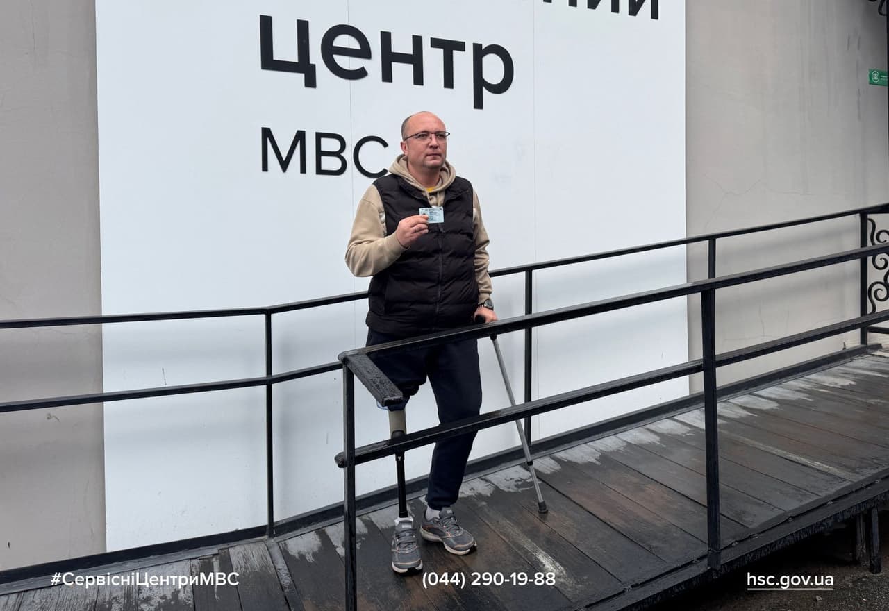 Людина з протезом ноги та милицею стоїть на пандусі біля будівлі, тримаючи посвідчення. На задньому плані — вивіска «Центр МВС» українською мовою. Сцена демонструє доступність державних сервісів для людей з інвалідністю та підкреслює інклюзивність інфраструктури.