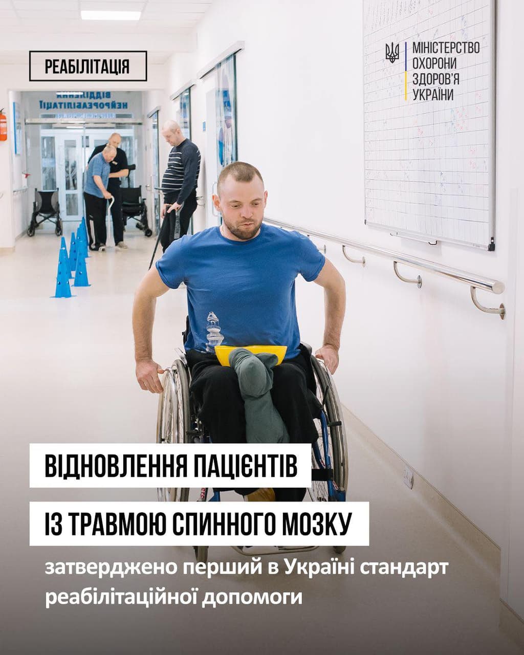 A man in a wheelchair moves through a rehabilitation facility, navigating between blue cones placed on the floor as part of a physical therapy exercise. The hallway features a large chart and signage in Ukrainian, including the logo of the Ministry of Health of Ukraine. The text announces the country’s first official rehabilitation standard for patients with spinal cord injuries. The scene emphasizes structured recovery, accessibility, and institutional support.