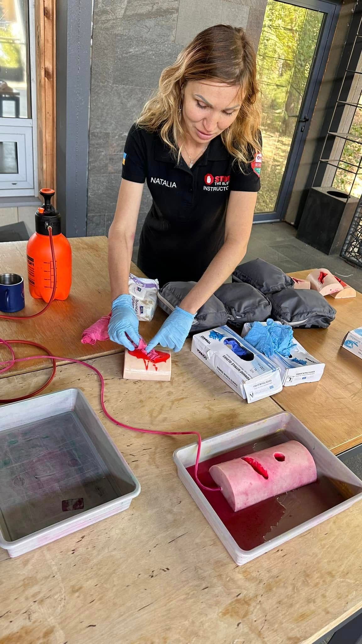 A girl in gloves stands by a table with training models for providing assistance in case of injuries.