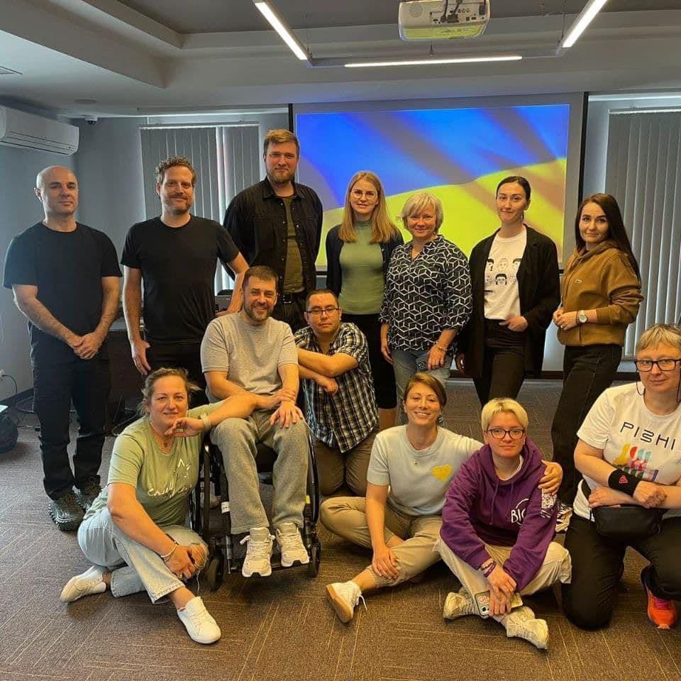 A group of people poses for a photo in a hall, with a projector displaying the Ukrainian flag, expressing gratitude to international partners for their support in implementing crucial initiatives for people with disabilities.