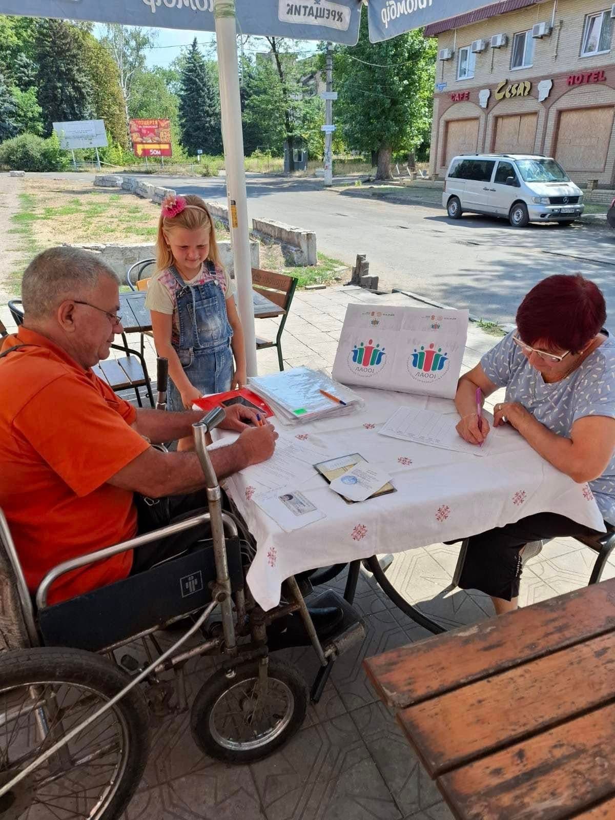 A man, woman, and girl sitting at a table under an umbrella outdoors.