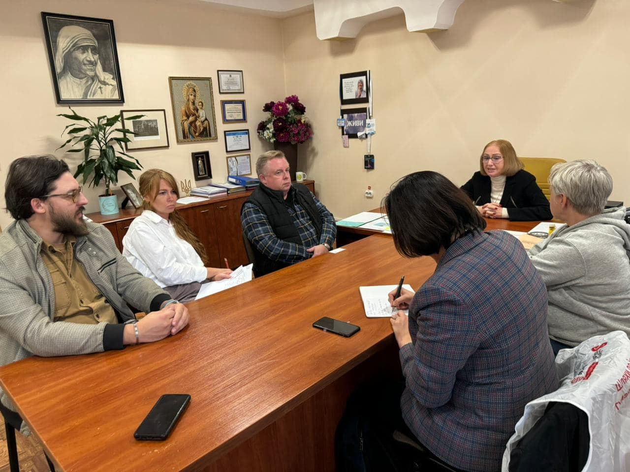 Six people are sitting at a table in an office, with one of the women taking notes.
