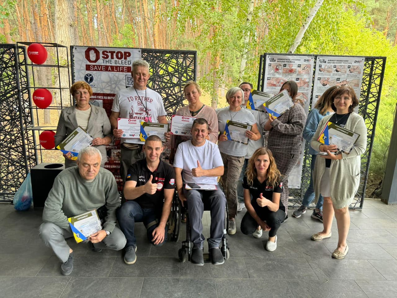 Training participants posing for a group photo against a backdrop of posters and a forest in the background.