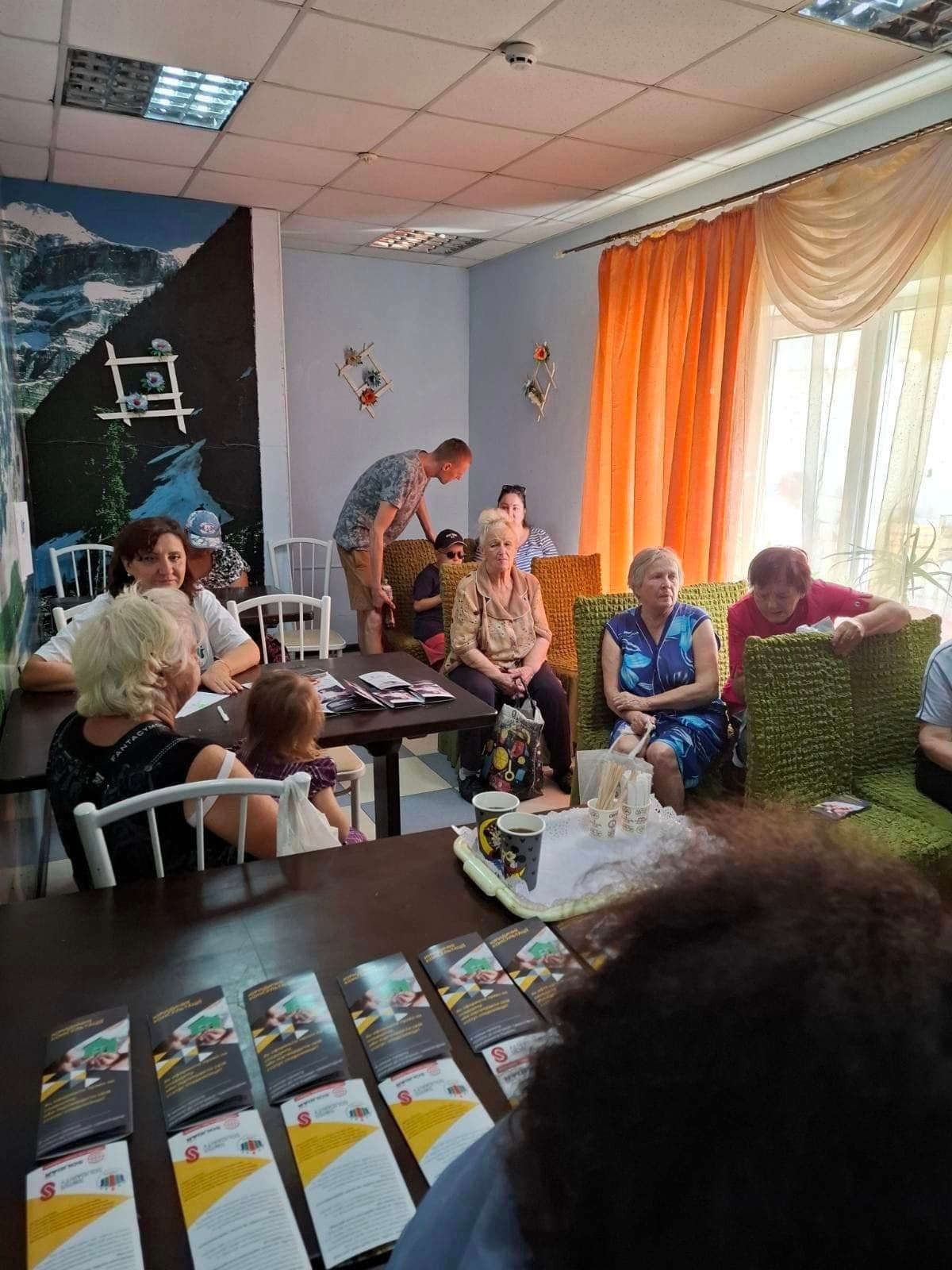 Жінки сидять в залі перед столом, на якому розкладені листівки.