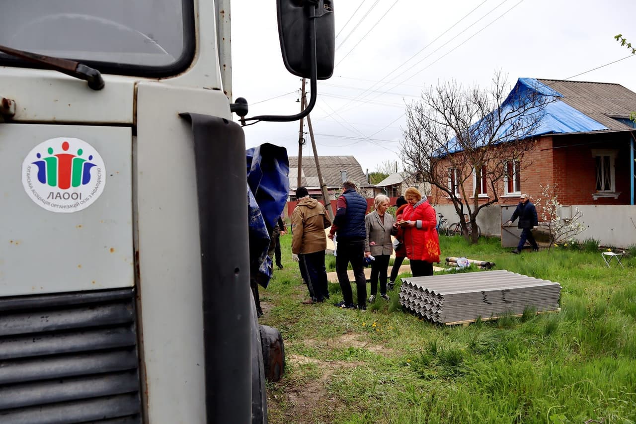 Волонтери роздають шифер і будівельні матеріали для відновлення пошкоджених будинків. На передньому плані — вантажівка з логотипом ЛАООІ.