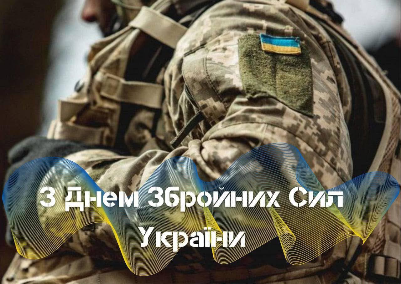 A close-up image shows a military camouflage uniform with tactical gear and a Ukrainian flag patch on the shoulder. The background is blurred, focusing attention on the uniform. Overlaid is a decorative wave in blue and yellow with white text reading “Happy Armed Forces Day of Ukraine.” The scene honors and celebrates Ukrainian military personnel on their professional holiday.