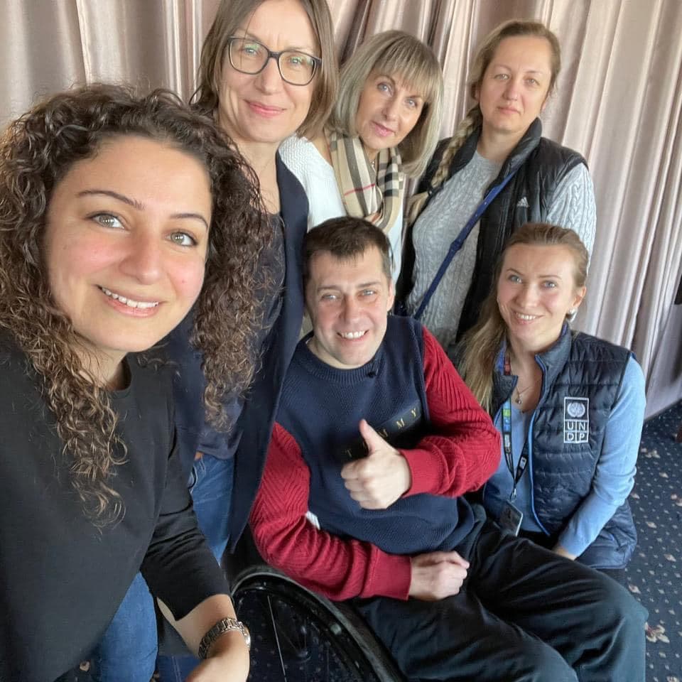 A group photo of five women and a man in a wheelchair, with three women and the man smiling.