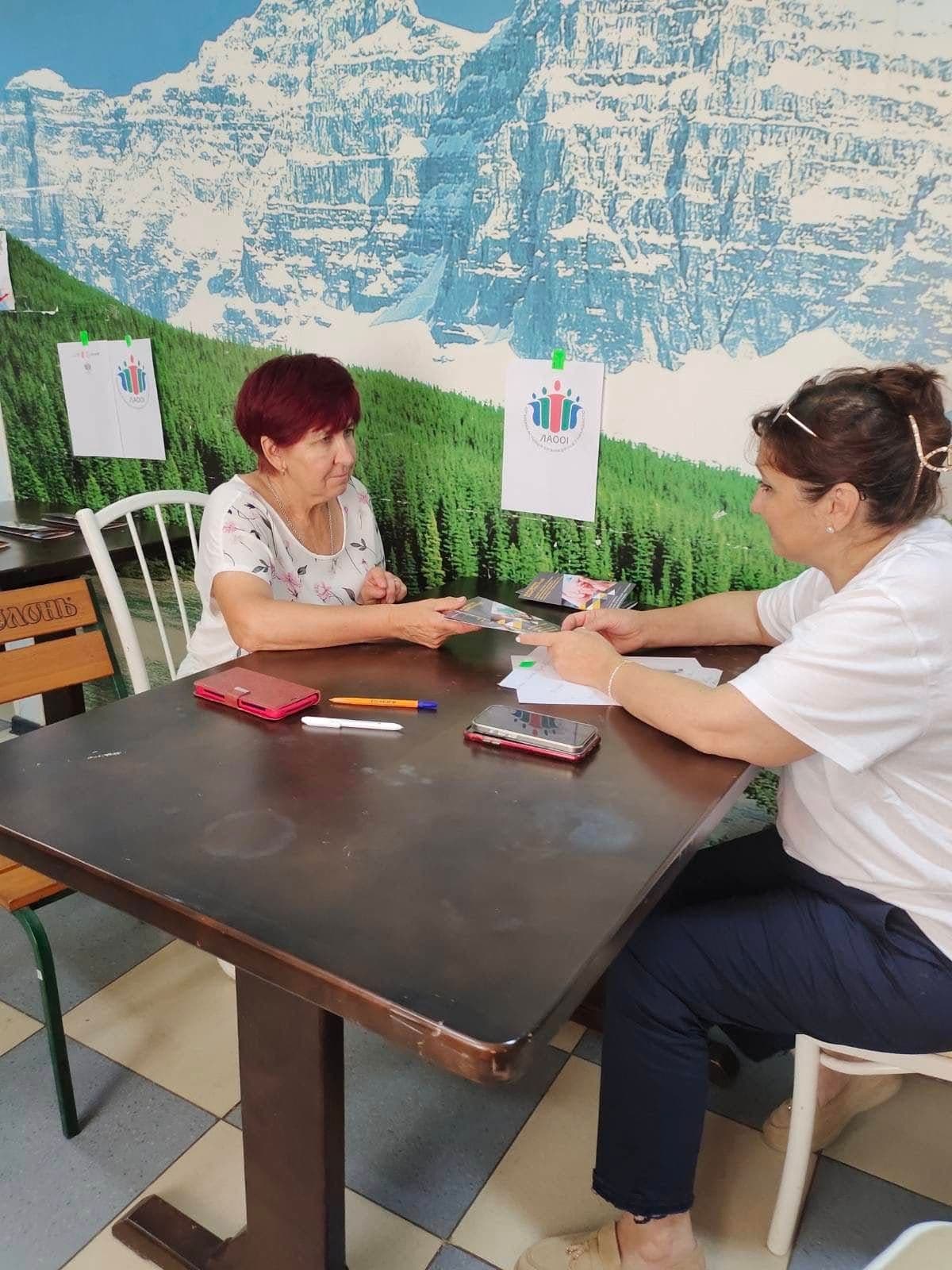 Дві жінки сидять за столом і тримають листок.