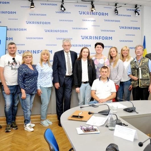 A group photo in a hall with an oval table in front of a "Ukrinform" banner.